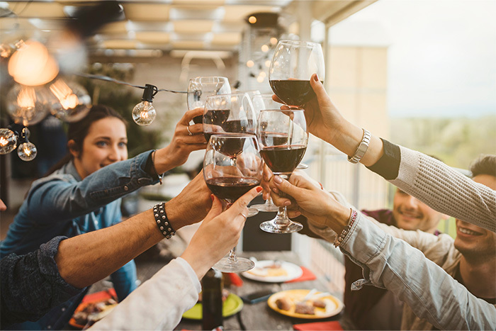 People around a table holding up cheers with red wine glasses