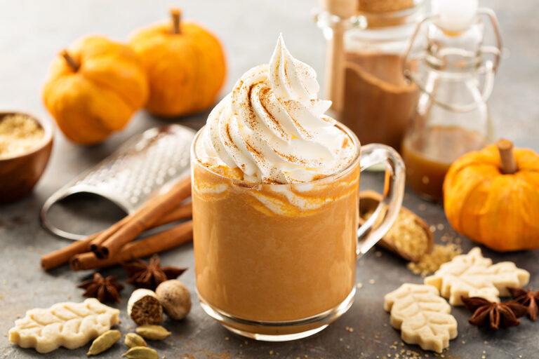 Pumpkin spiced latte in a clear mug with whipped cream by fall décor