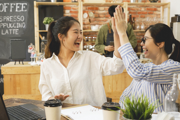 Two women high fiving at a cafe.