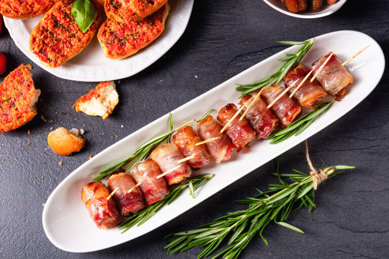 Bacon wrapped dates on a long serving plate garnished with rosemary.