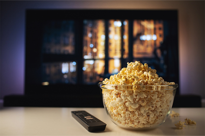 A bowl of popcorn next to a TV remote
