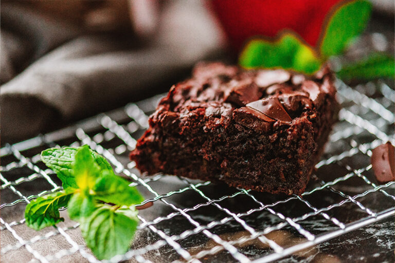 A square piece of chocolate cake on a cooling rack beside mint.