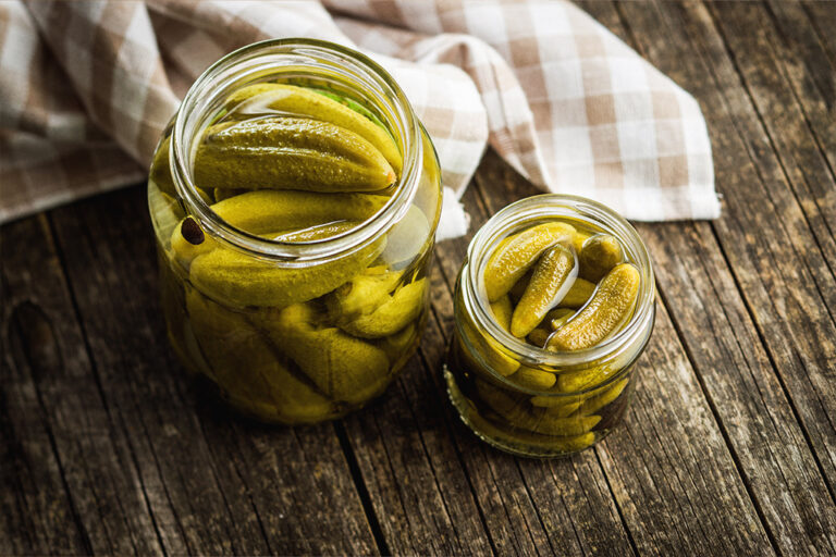 Two dill pickle jars on a wooden table.