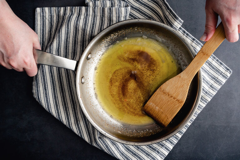 An individual stirring and browning butter in a stainless steel pan.