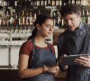 Two restaurant employees reviewing orders on a tablet.