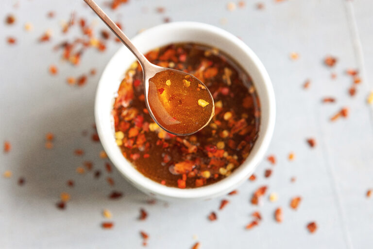 A small spoon dipping into a ramekin of spicy maple syrup.